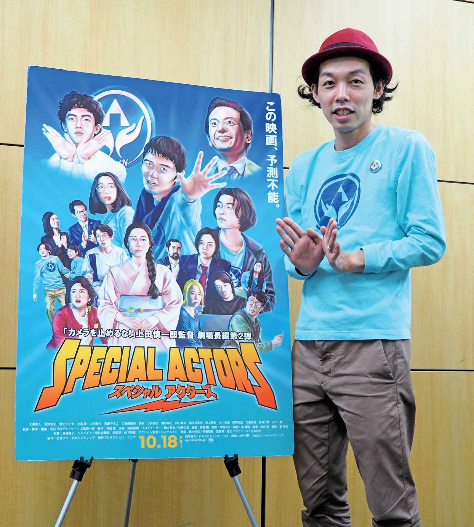 『スペシャルアクターズ』日本版劇場公開ポスターと上田慎一郎監督。このポーズと水色ロングTシャツの意味するところは、映画を見てのお楽しみ。